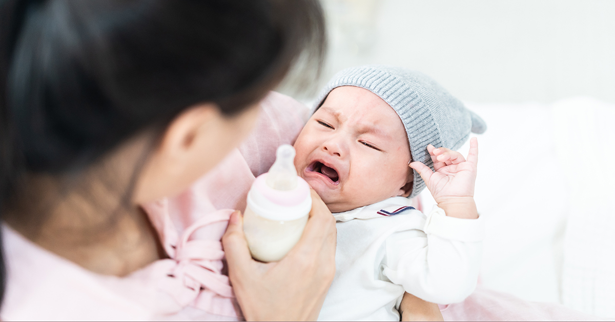 Asian mother holding and feeding cute newborn baby from milk bottle